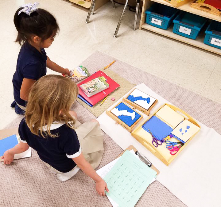 Two students sit on floor working together on a Montessori material