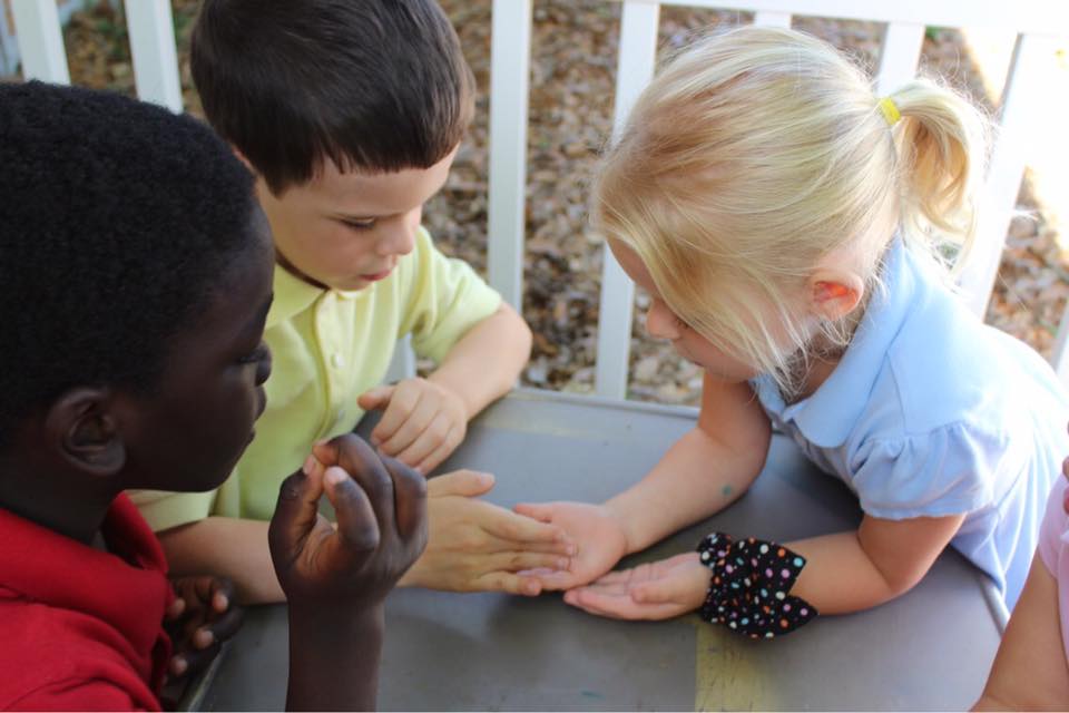 Three students huddle together with hands out examining something one student is showing