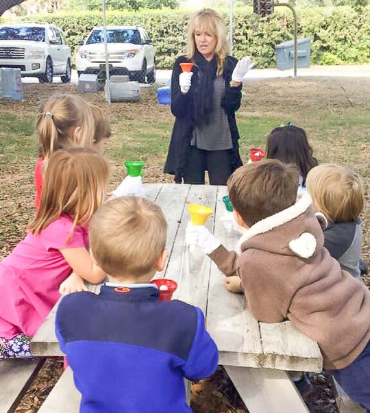 Teacher stands to show students a hand bell demonstration