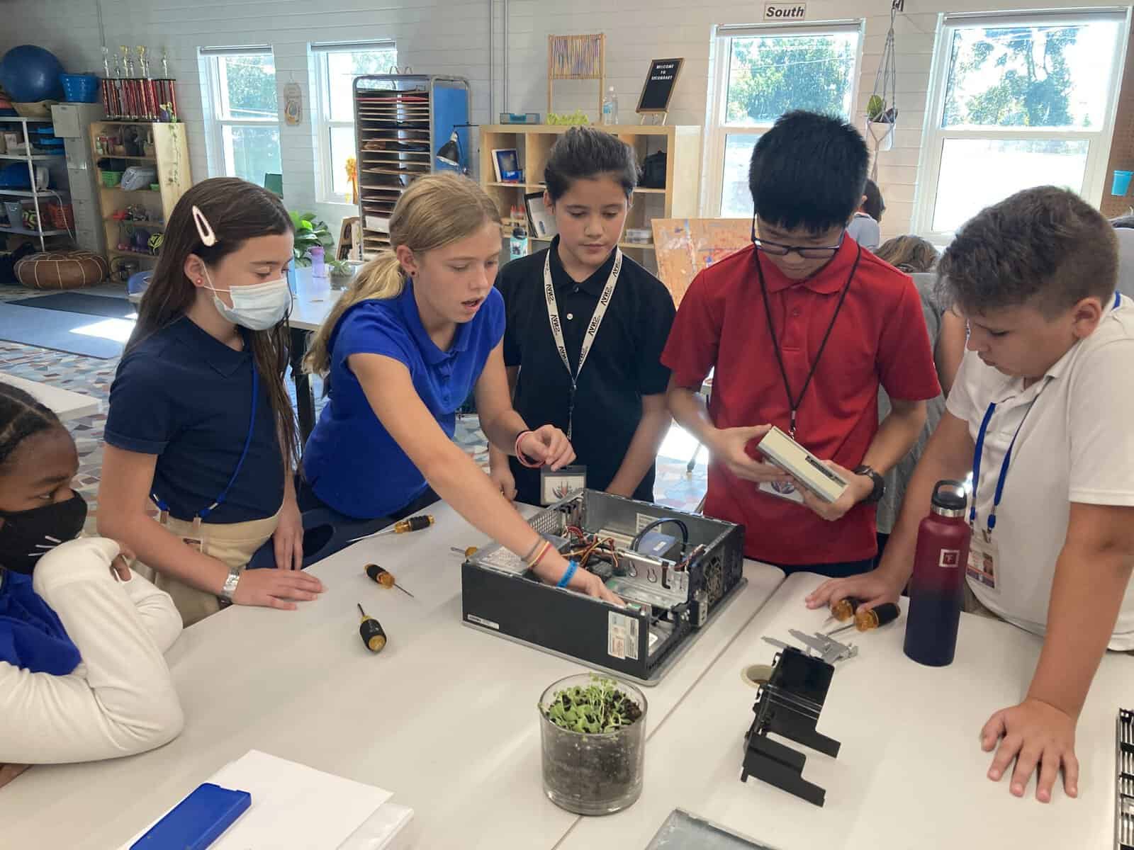 Students work around a computer that has been disassembled.